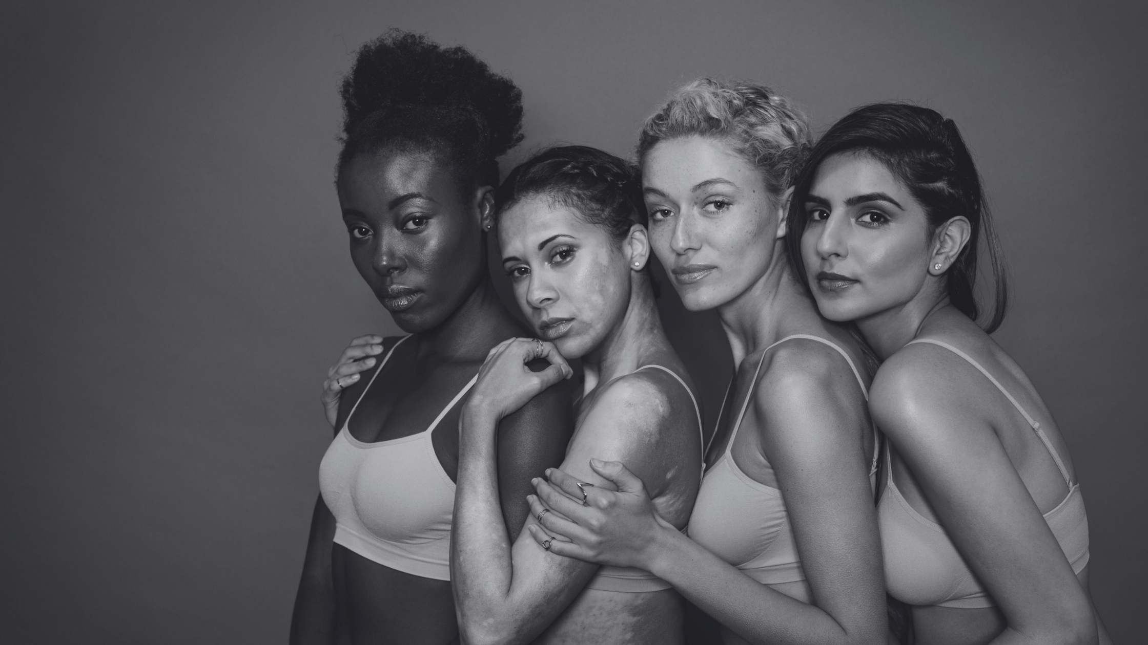 Black and white photo of four women standing close together against a gray background